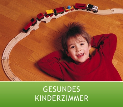 Lachender Junge in gesundem Kinderzimmer auf Parkett liegend vor Holzeisenbahn